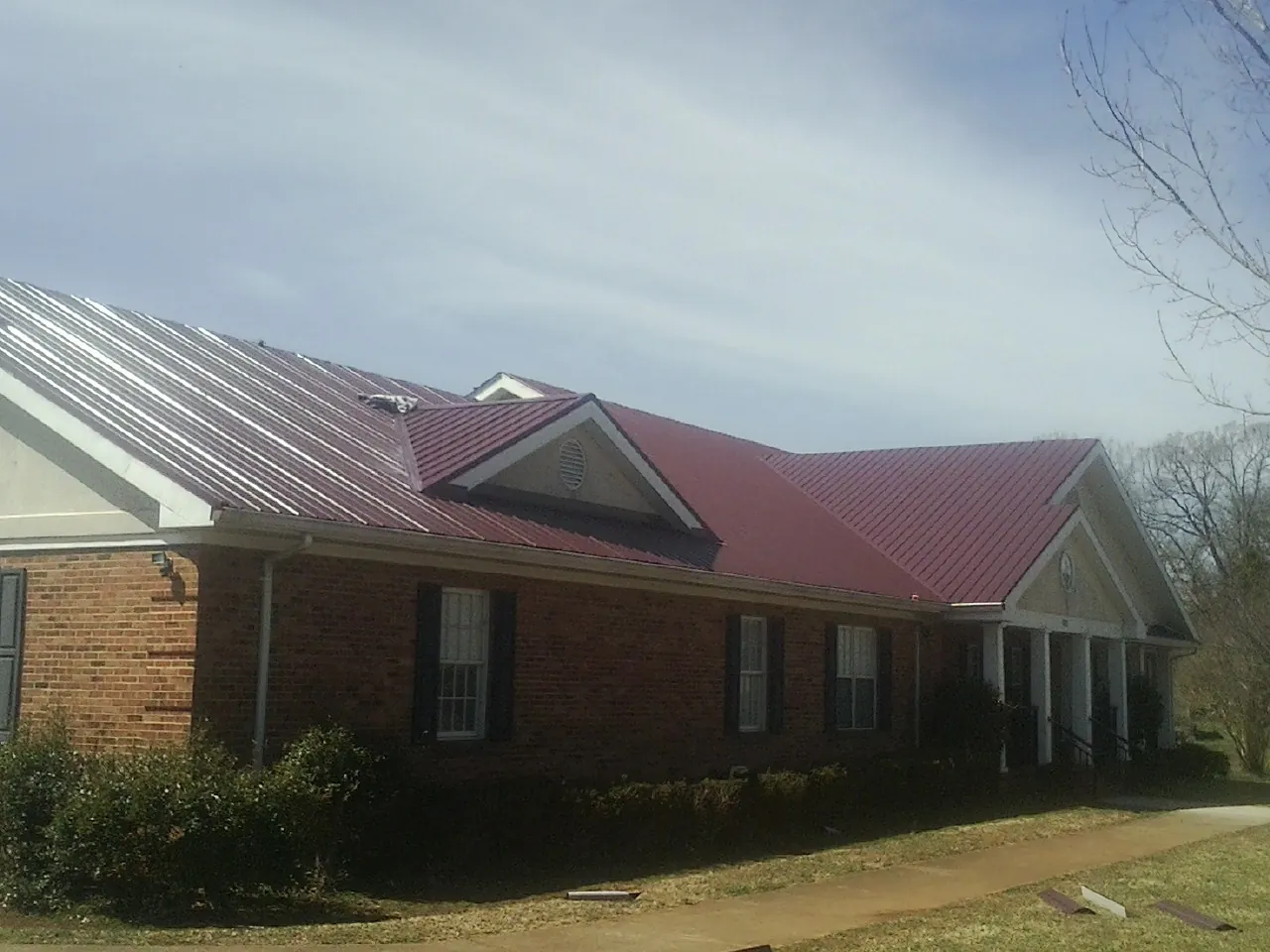 Red metal roof with gabled entries on a long brick building, from a Hail Damage Roof Repair job in Afton