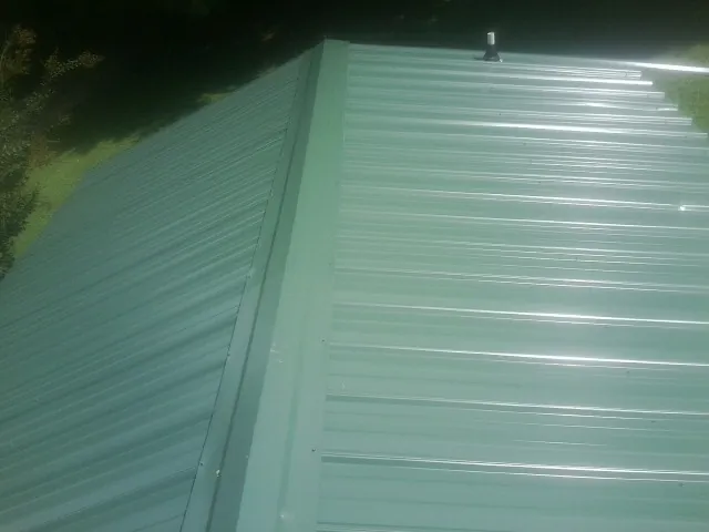 New green metal panels meeting at the ridge of a roof — Flat Roof Repair work by our crew in Afton